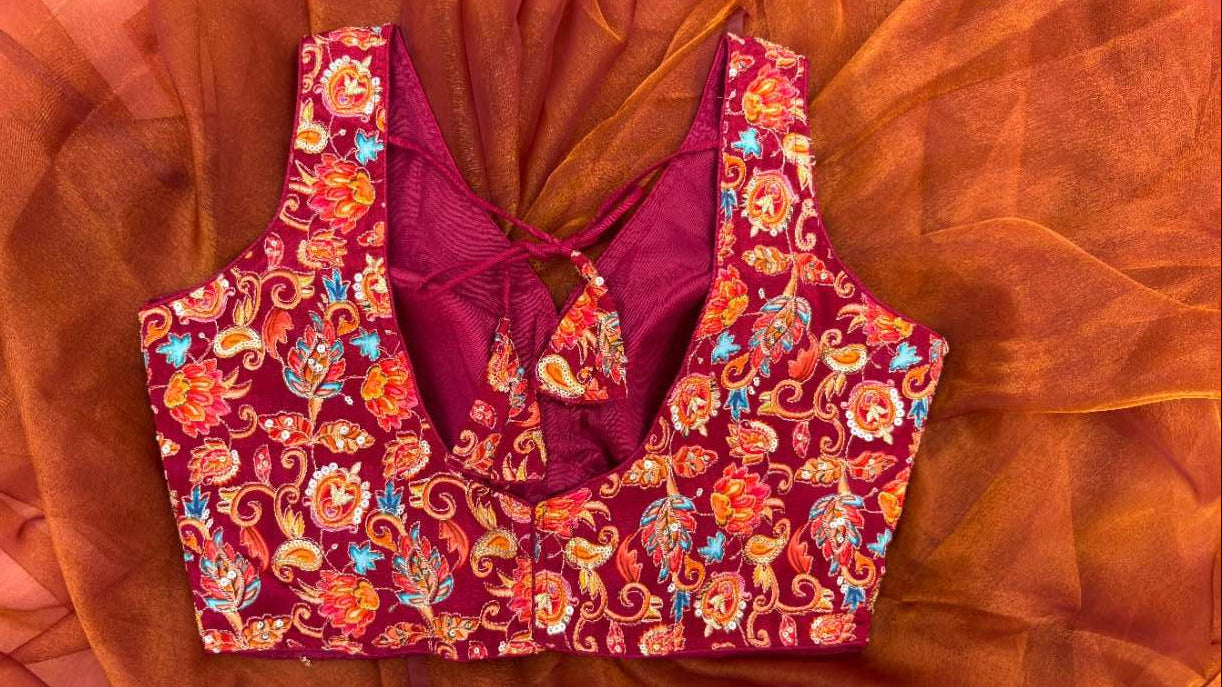 Back view of the Rang Mahal Blouse showcasing adjustable dori tie-up closure. The sleeveless maroon crepe blouse with vibrant floral embroidery offers a customizable fit and elegant styling for weddings, parties, and festive occasions