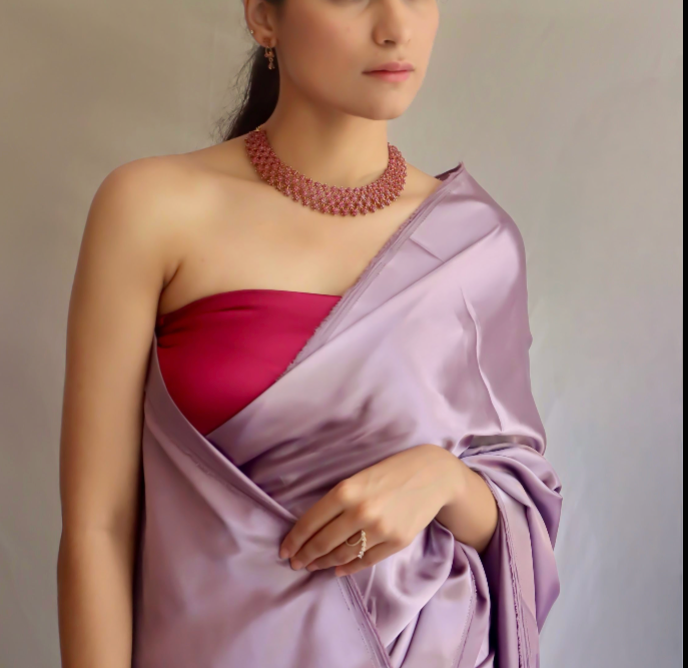 Woman wearing a purple saree with a contrast blouse and necklace against a neutral background