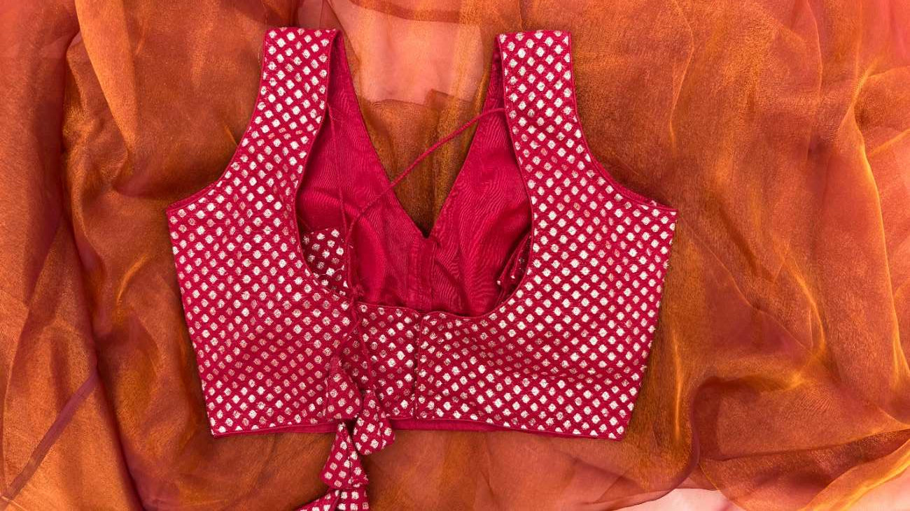 Back view of Anaira Crimson Diamond Blouse showing a dori tie-up closure. The sleeveless V-neck blouse in deep red brocade with silver diamond motifs combines traditional charm with modern styling and offers a customizable fit for weddings and festive occasions.