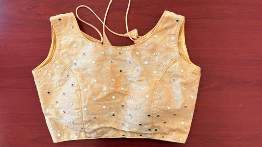 Front view of Label Anaira’s Noorika Mirror Blouse in a soft cream silk blend. The sleeveless design features delicate mirror work scattered across the front panel, catching the light beautifully. The minimal pattern and smooth finish make it an elegant choice for festive or contemporary saree looks