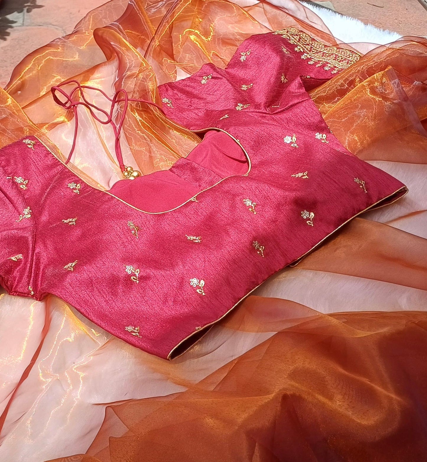 A side view of a red blouse with gold thread work under sunlight