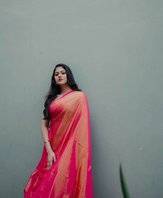 Woman wearing a pink linen tissue saree against a gray background, the saree is soft and affordable
