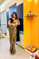 Woman in a gold saree standing in a decorated room with flowers.