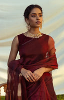Woman wearing blood red  saree with gold jewelry against a neutral background