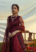 Woman in blood red organza saree with jewelry against a scenic background