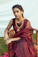 Woman in a blood red organza saree with gold jewelry sitting outdoors.