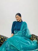 Woman in Ocean Blue Organza Sareesitting on a decorative chair with a white background