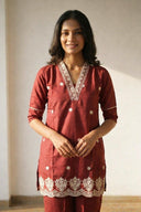 Woman wearing a red traditional outfit with white embroidery against a plain background