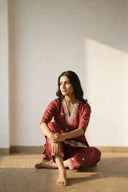 Woman in a red traditional outfit sitting on the floor against a plain wall.