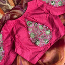 Close-up of a pink embroidered blouse with green patterns on a brown fabric background