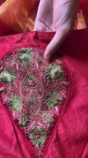Close-up of a hand holding a piece of red fabric with intricate green embroidery.