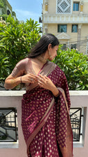 Woman wearing Marron Plum classic saree with a building and greenery in the background