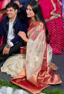 Shriya in Classic Red Banarasi Saree sitting next to Dhruv in formal attire with a colorful background.