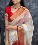 Woman wearing a red blouse with a white saree featuring gold patterns against a dark background