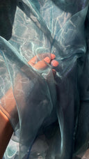 Close-up of a person's hand with sheer blue fabric draped over them.