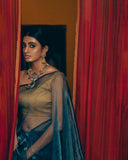 Woman in traditional aDark Blue Organza with jewelry, standing behind red curtains.