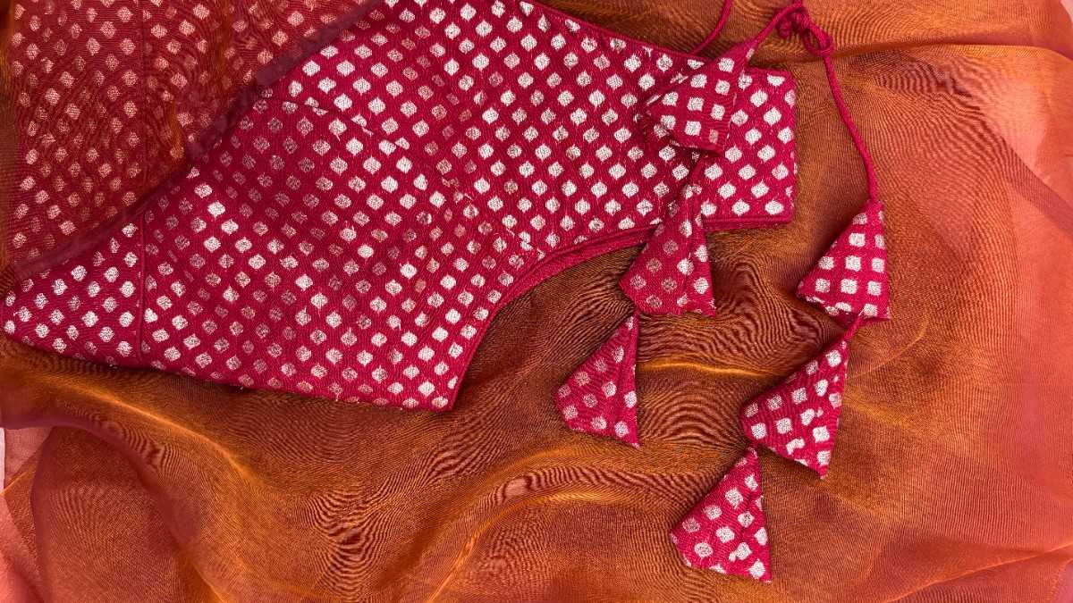 Close-up of deep red brocade fabric of the Anaira Crimson Diamond Blouse showcasing finely woven silver diamond (paisley) motifs. The detailed texture and subtle shimmer highlight premium craftsmanship and make it suitable for festive and wedding sarees.