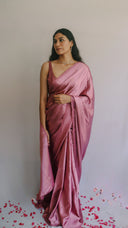A bridesmaid wearing a pink satin saree with mauve undertone , minimal accessories with petals near her