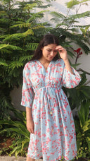 Woman wearing  Bougenvillea dress standing in front of green foliage.