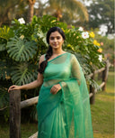 Woman in a shining green organza saree standing outdoors with greenery in the background