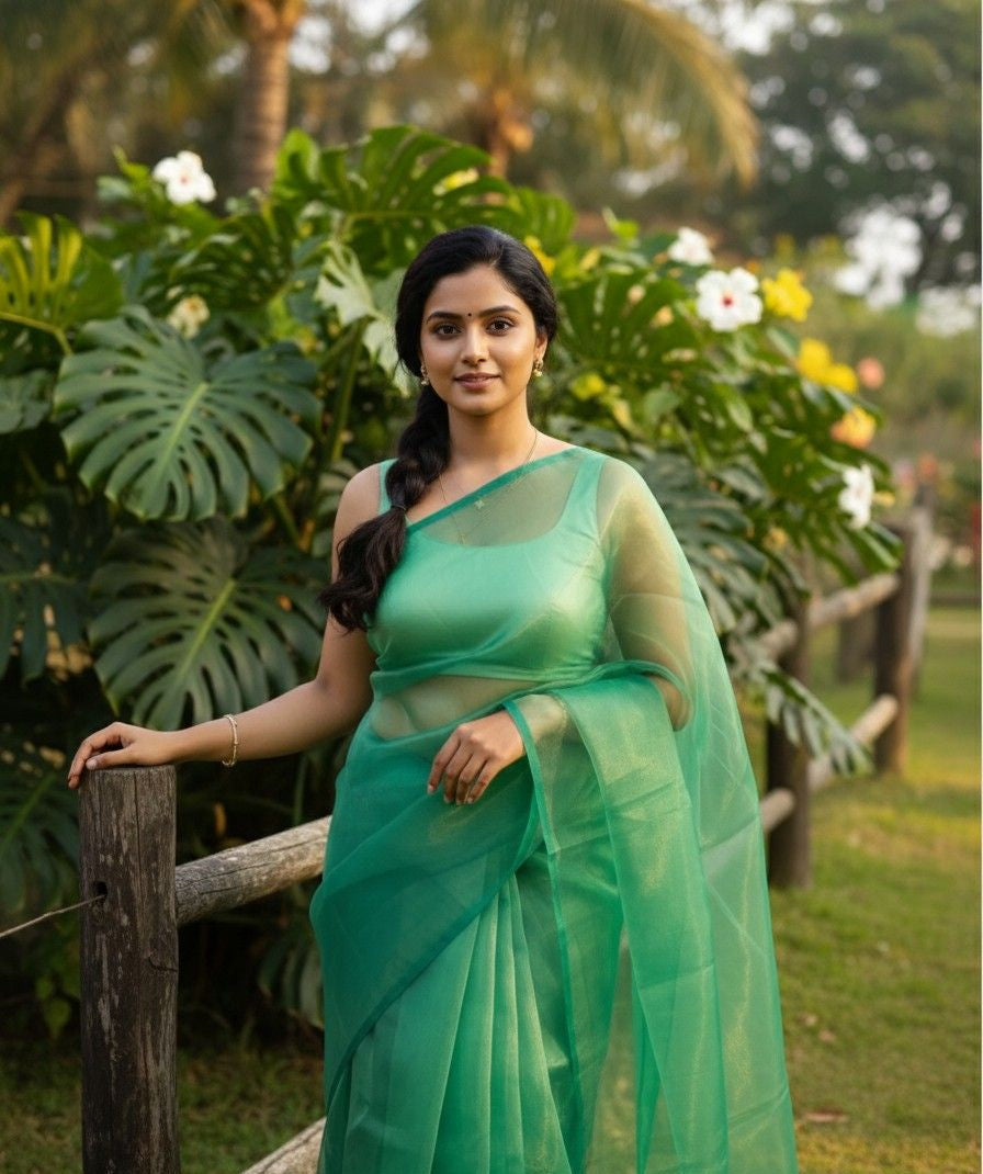Woman in a shining green organza saree standing outdoors with greenery in the background