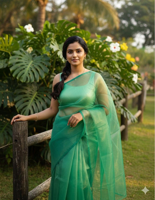 Woman in a shining green organza saree standing outdoors with greenery in the background