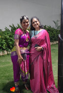 Two women in sarees, older woman wearing reversible saree standing outdoors with greenery