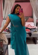 Woman in a teal organza saree taking a mirror selfie in a bedroom.