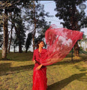 Woman in a red organza saree standing outdoors with trees