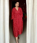 Woman wearing a red free size dress  with pockets standing in a doorway.