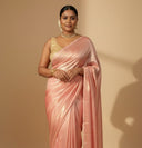 Dusky indian woman wearing pink shimmer saree of satin silk material, looking traditional in front of a minimal beige background.