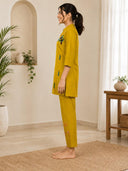 Woman wearing a mustard yellow outfit with green patterns in a home setting.