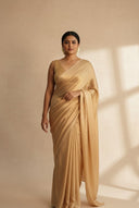 Woman wearing gold shimmer satin silk saree that pleats softly in a biege background with a traditional hairstyle