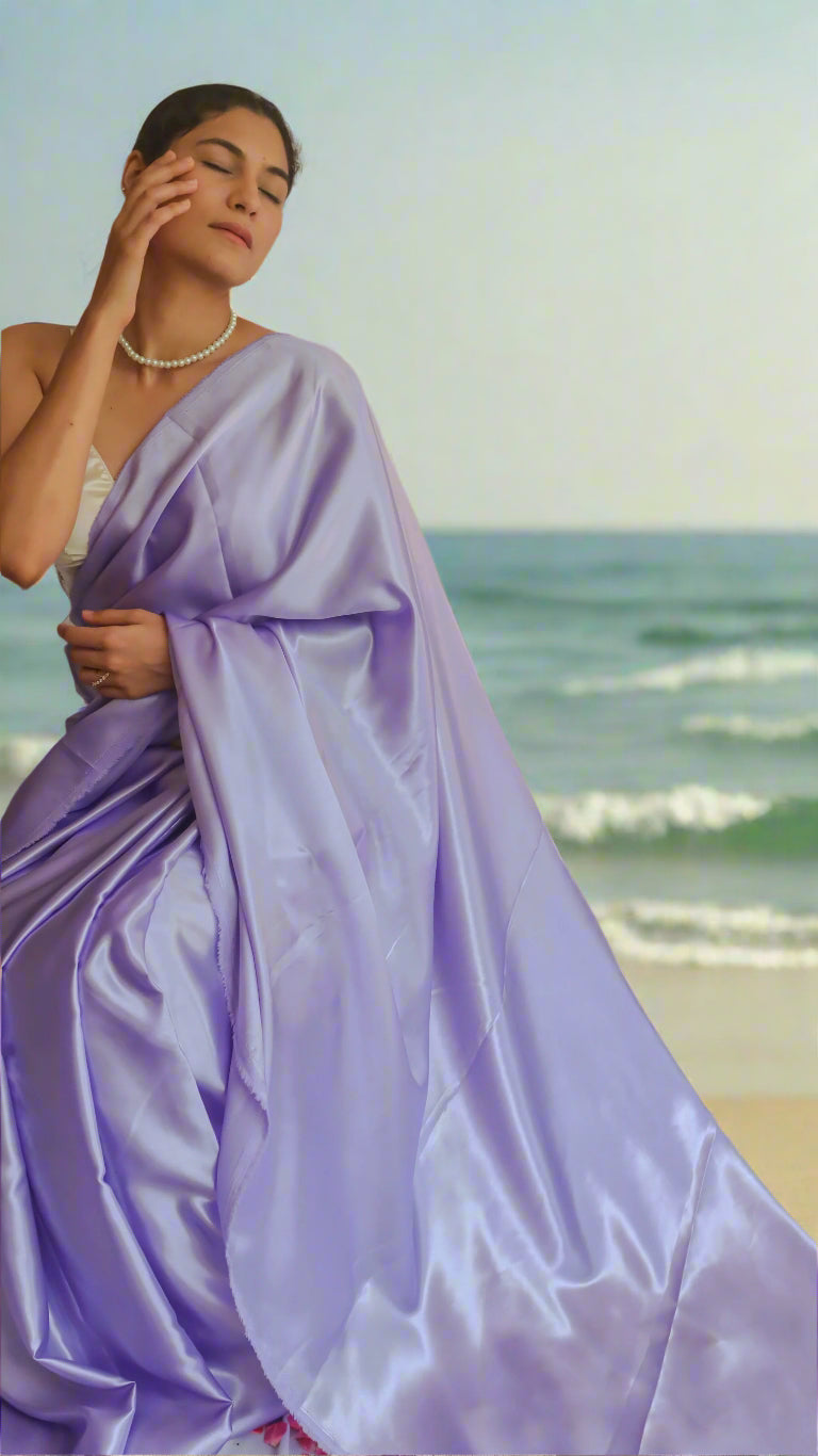 A woman seated wearing a lavender satin saree