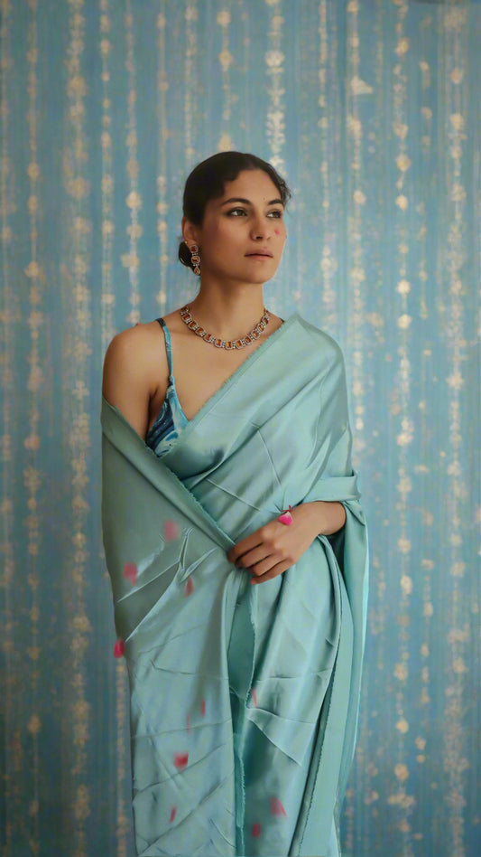 A woman wearing a mint blue satin saree with a teal blouse