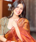 Woman wearing an orange with gold shine organza saree paired with a green blouse, beautifully styled with drop earrings and jumkas