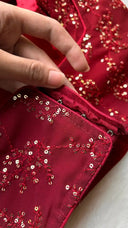 Close-up of a hand touching red fabric with gold embroidery on a white background