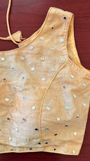 Beige sleeveless top with decorative buttons on a wooden surface