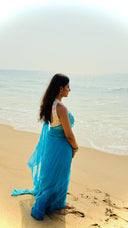 Woman in a blue saree standing on a beach with ocean in the background
