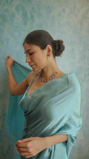 A woman wearing a mint blue satin saree showing detail of saree and jewellery