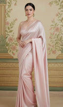 Woman wearing a light pink pastel satin saree with a decorative background