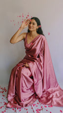 A woman seated wearing a pink satin saree with matching blouse