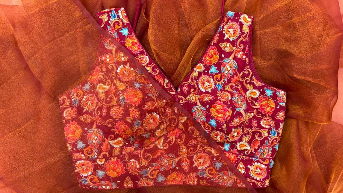 Styled look of the Rang Mahal Blouse paired with a festive honey queen bee saree. Sleeveless maroon crepe blouse with dori tie-up back, rich multicolored floral embroidery, and subtle shine create a luxurious and elegant ensemble for weddings, parties, and traditional celebrations.