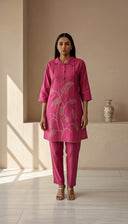 Woman wearing a pink outfit with floral patterns in a minimalistic room.