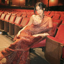 Woman in honey vine organza sareesitting in an empty theater with red seats.