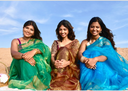 Three women in organza sarees sitting together with a clear blue sky in the background