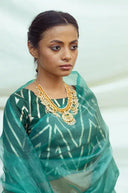 Model wearing Teal Organza Sareewhite patterns and gold jewelry against a light background