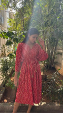 Woman in a red patterned dress standing outdoors with greenery around