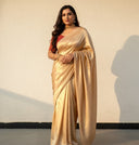 Woman wearing a gold saree shining under sunlight with a contrast red blouse against a plain white textured background