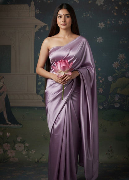 Woman in a lavender saree, purple satin saree, flowy saree, holding a pink flower against a decorative background